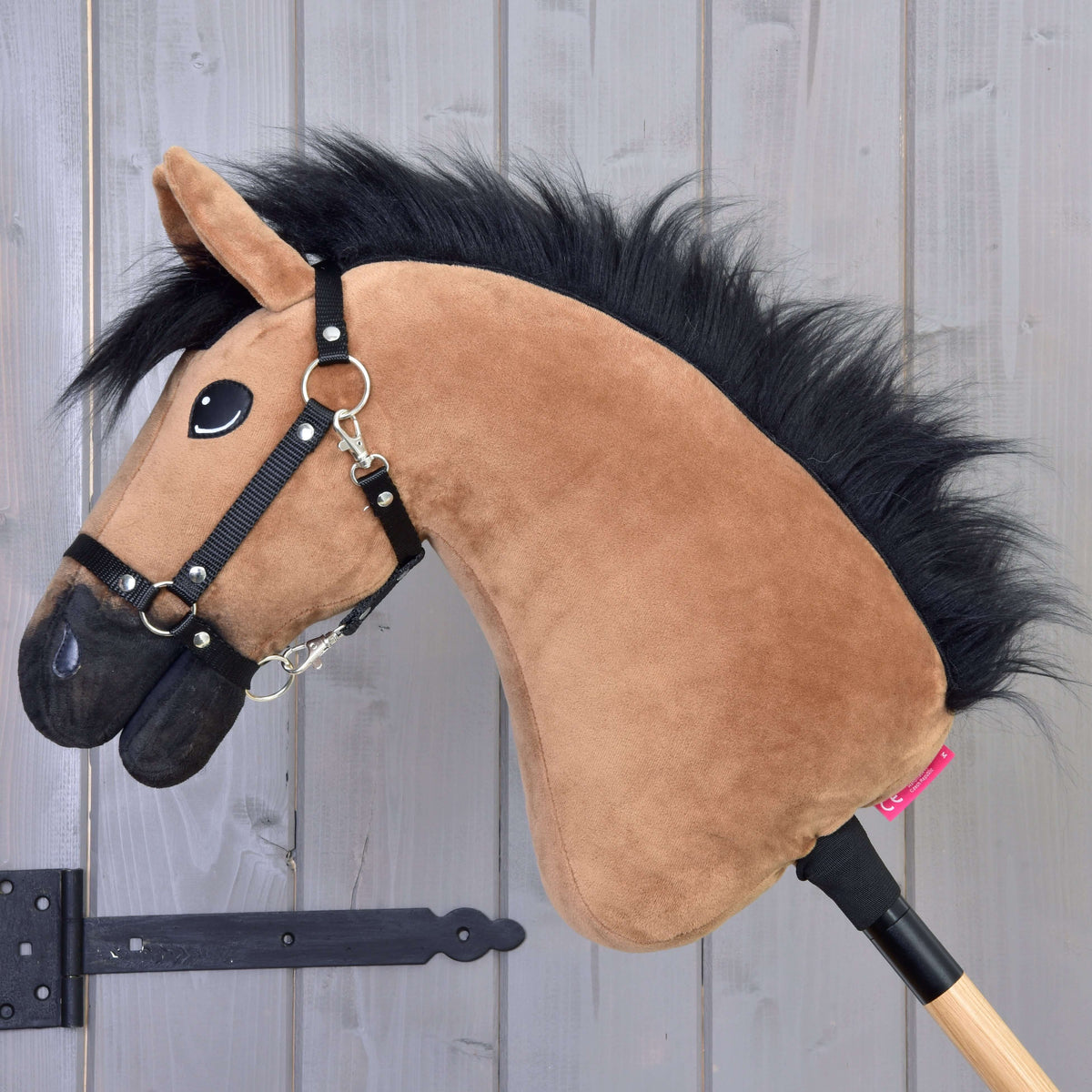 Side view of the light brown Hobby Horse with a fluffy black mane, black muzzle and black halter on a stick