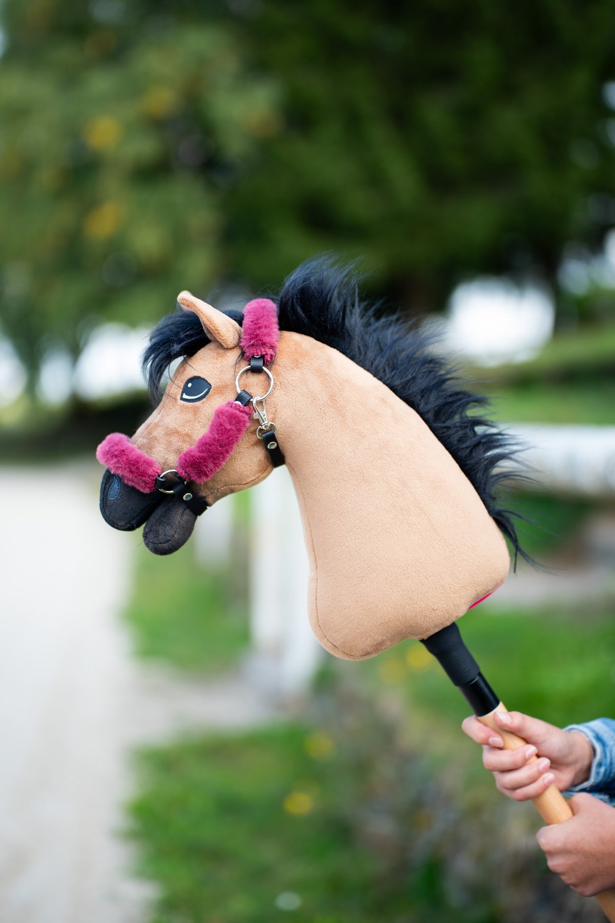 Hobby Horse Cookie málnarózsaszín szőrmés fekete kötőfékben, bozontos fekete sörénnyel, fák előtt a magasba tartva