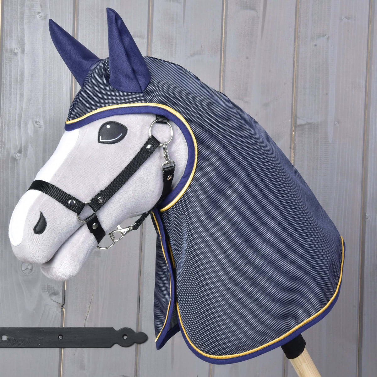 Szürke Hobby Horse ló fekete kötőfékben, a fején és nyakán sötétkék esőtakaró fültakarókkal és arany paszpóllal