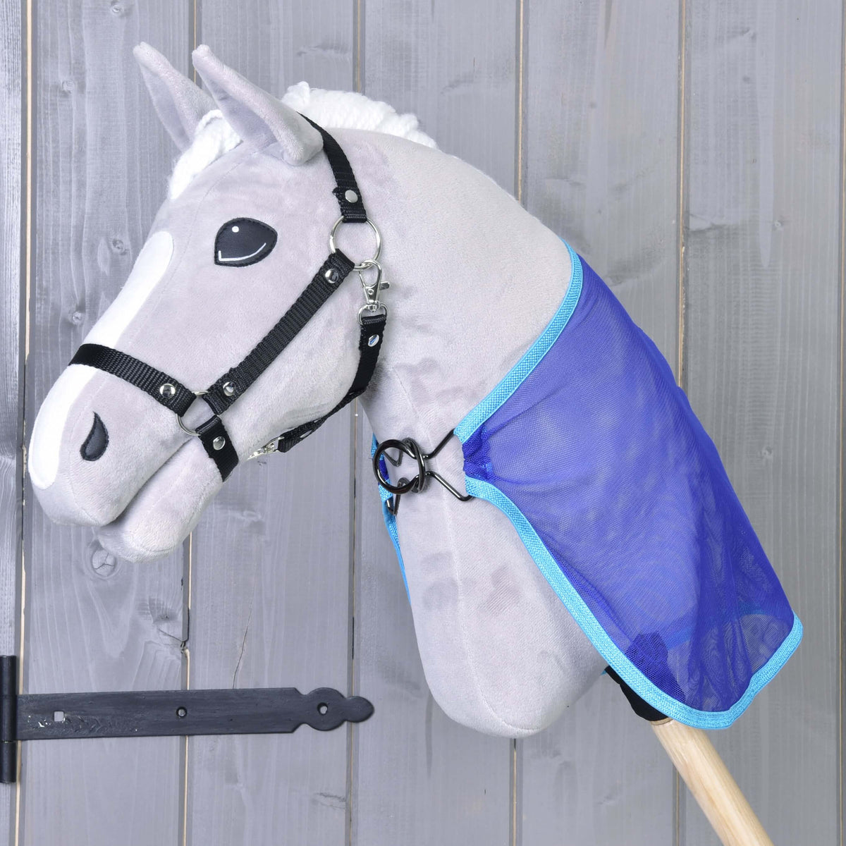 Szürke plüss Hobby Horse ló fekete kötőfékben, kék hálós légytakaróban, a mellén fémkarikával rögzítve