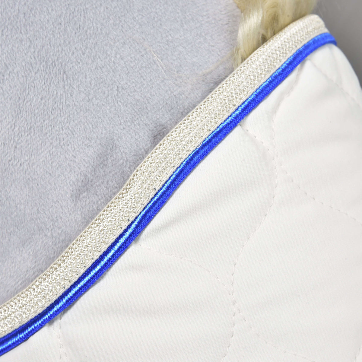 Close-up of the Blanket Cream Pearl neckline: royal blue piping and a shimmering beige braid edge on cream quilting