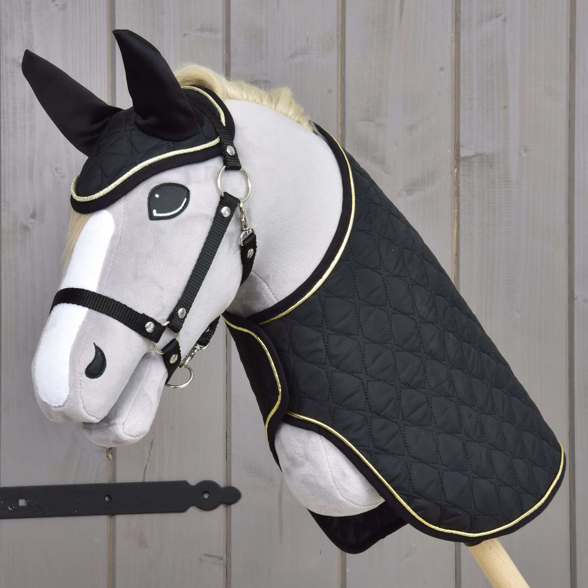 Grey plush Hobby Horse in a black halter wearing the black quilted blanket and ear bonnet with gold piping