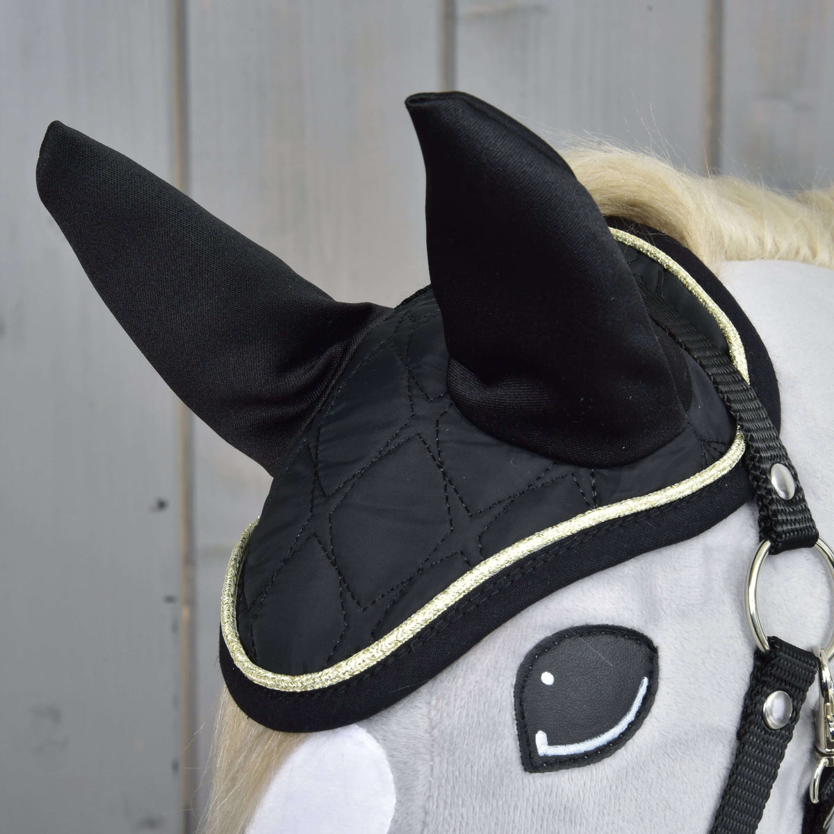 Close-up of the black quilted ear bonnet with black ear covers and glittering gold piping on a grey plush head