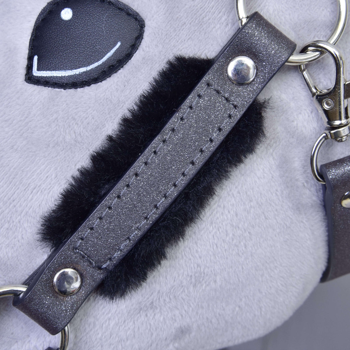 Close-up of the graphite cheekpiece over a black fur pad, with silver rivets and snap hook below the eye