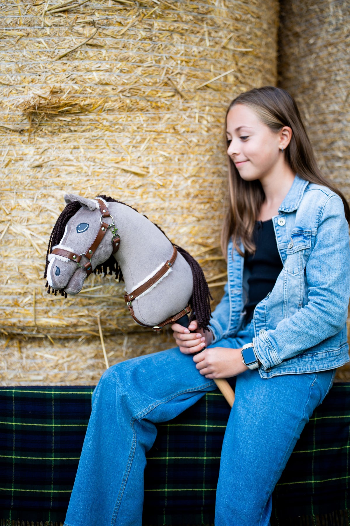 Girl in a denim jacket on straw bales holding Hobby Horse Guccini in a brown fur halter and matching breastgirth