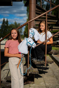 Two girls on an outdoor metal staircase holding white Hobby Horses in light blue halters, one with a lead rope