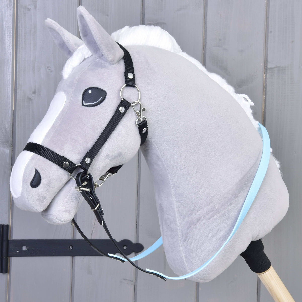 Szürke plüss Hobby Horse ló fekete kötőfékkel és az álla alatt bekapcsolt világoskék-fekete gumírozott kantárszárral