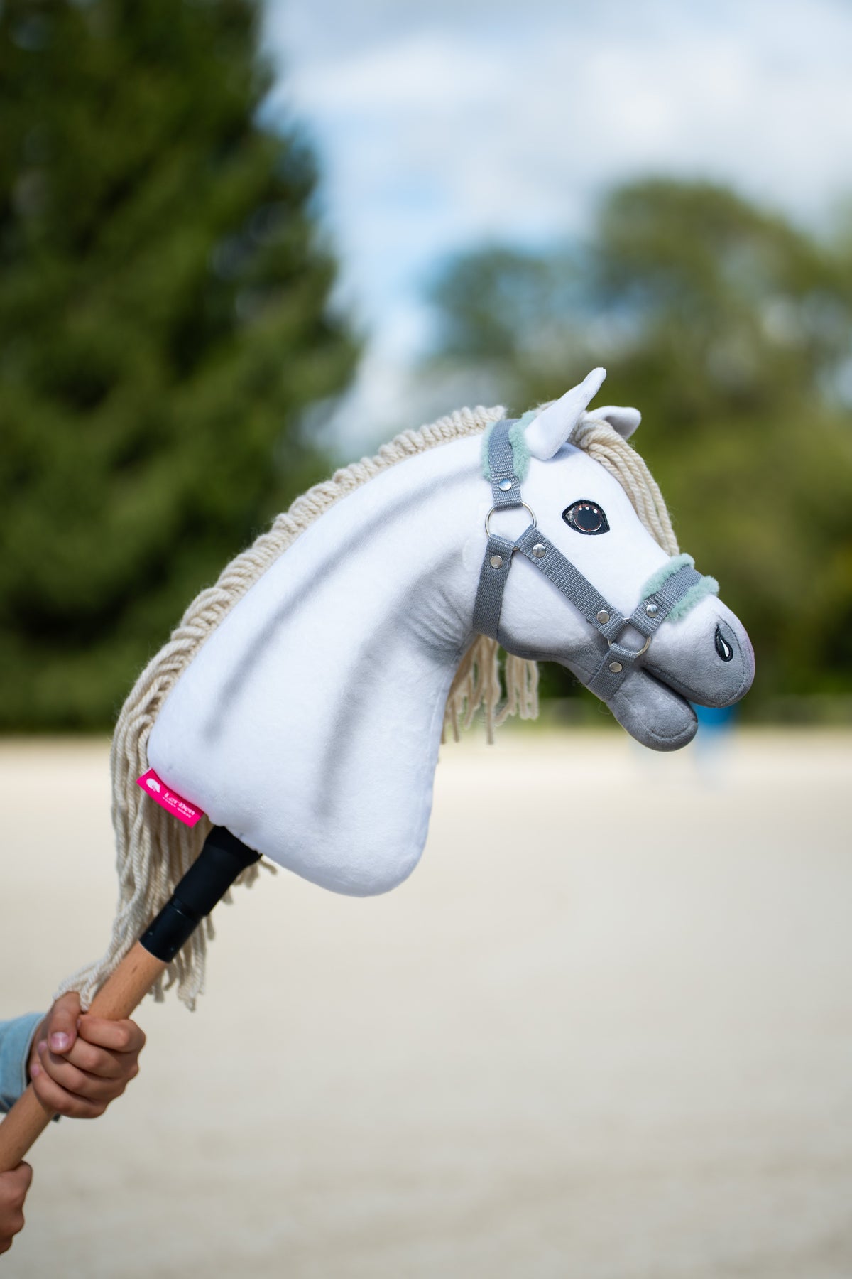 White Hobby Horse Little Lady with grey shading and a cream mane in the grey halter with mint fur, held up against trees