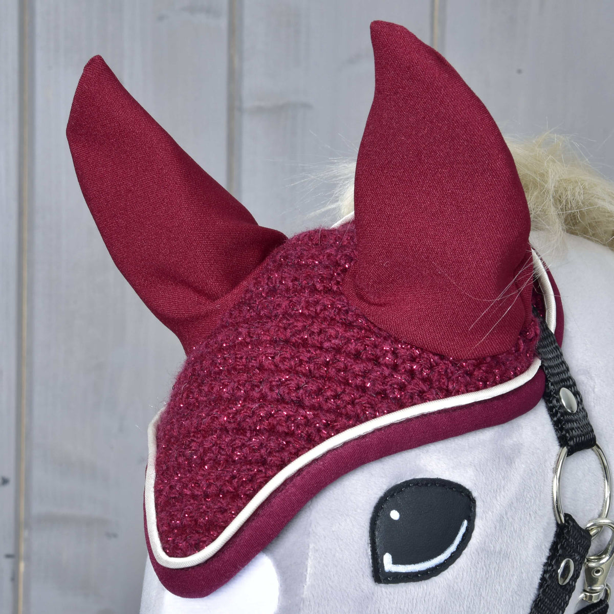 A horgolt Lux Maroon fülvédő közelről egy szürke Hobby Horse lovon: borvörös fülek, csillogó horgolás és fehér paszpól