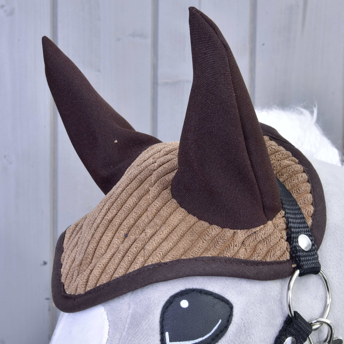 A világosbarna kordbársony fülvédő közelről sötétbarna fülekkel és szegéllyel egy szürke Hobby Horse lovon