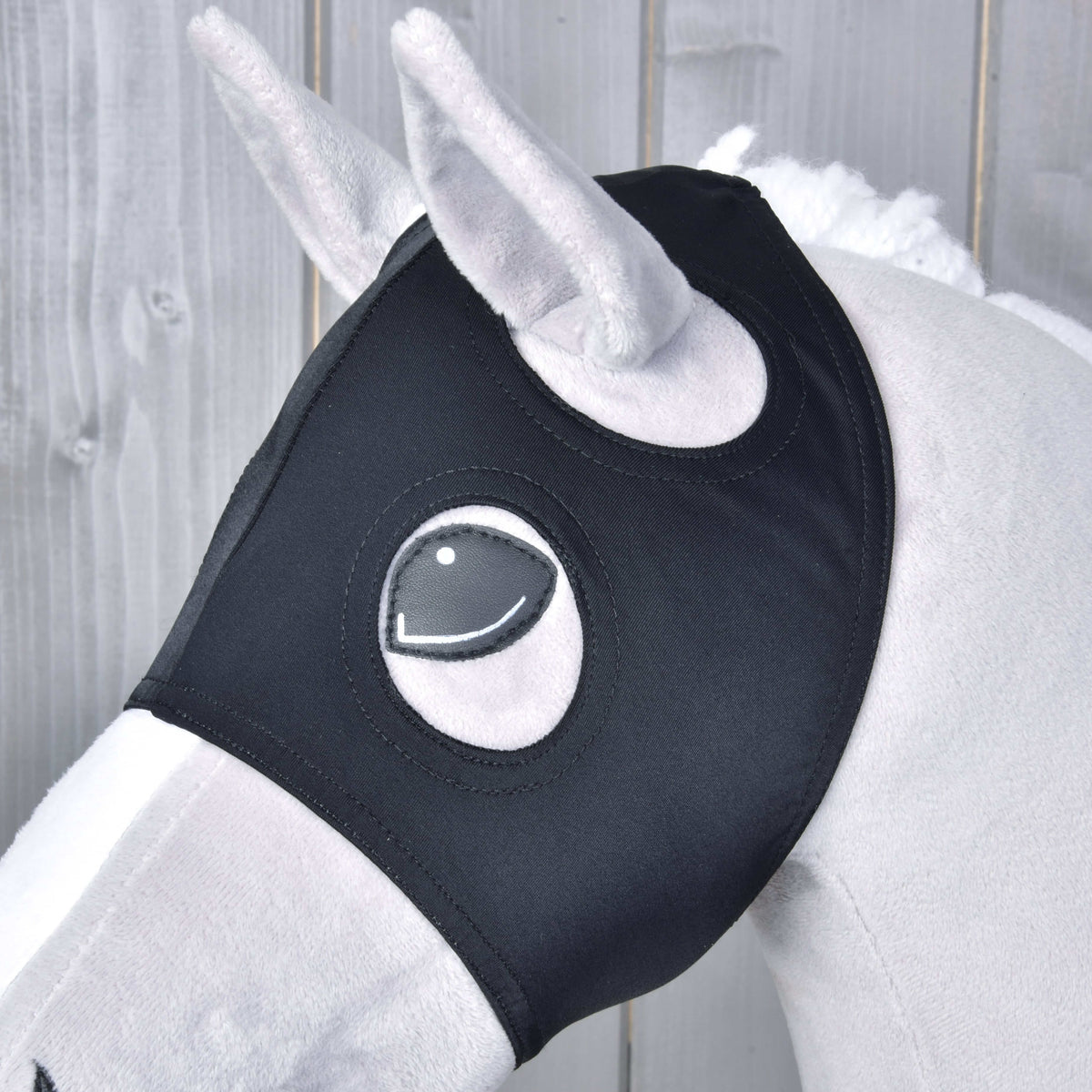 Close-up of the black mask on a grey Hobby Horse, the plush ear and stitched eye showing through the round openings