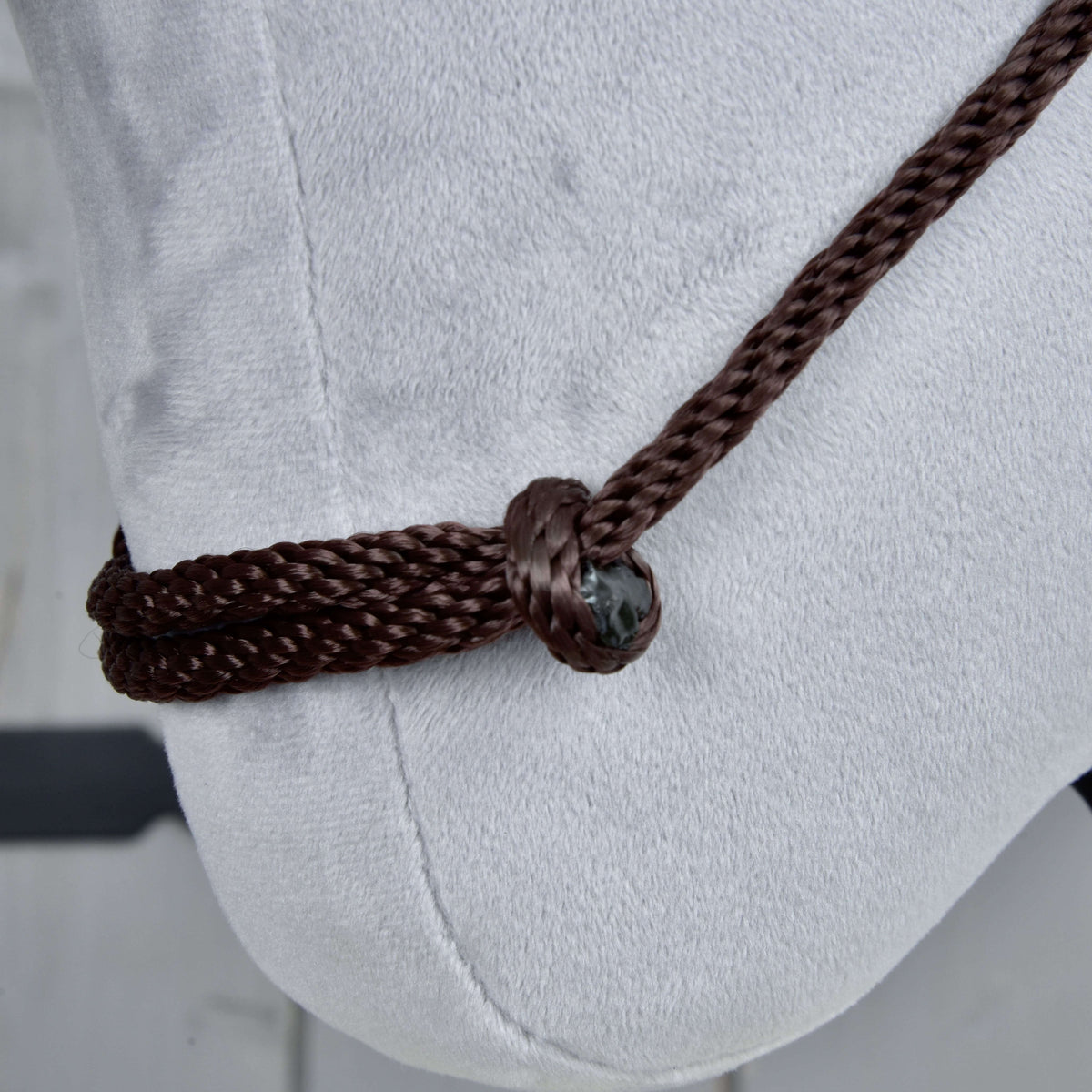 A Chocolate nyakgyűrű (cordeo) közelről a világosszürke plüssön: sötétbarna fonott kötél egy csomón átfűzve