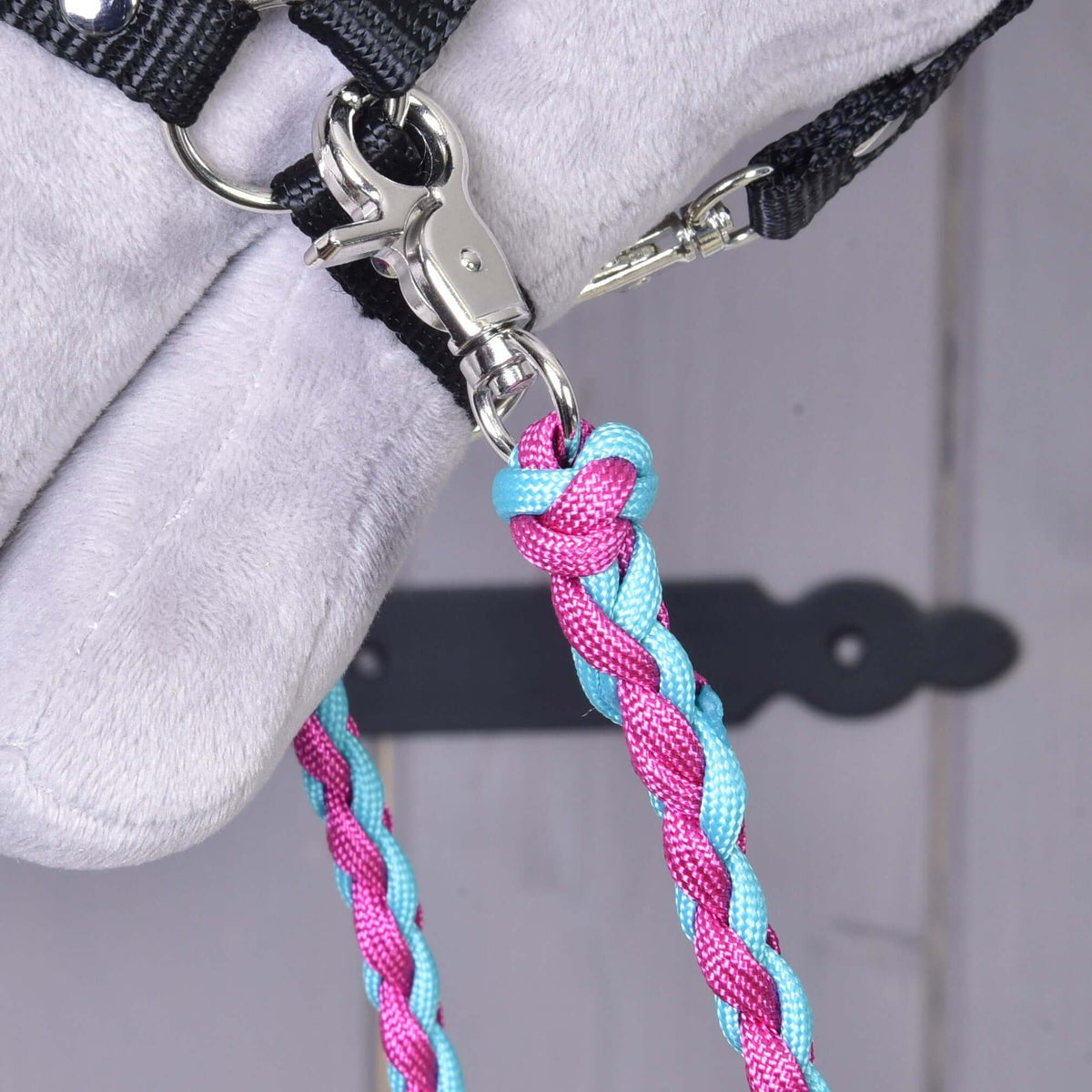 Close-up of a silver snap hook on the Reins knitted pinkie blue clipped to the ring of a black Hobby Horse halter