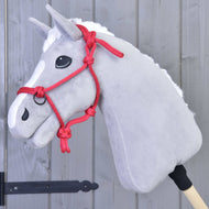 Fehér hókás, fehér sörényű szürke plüss Hobby Horse ló a piros csomózott kötőfékben, szürke fafal előtt