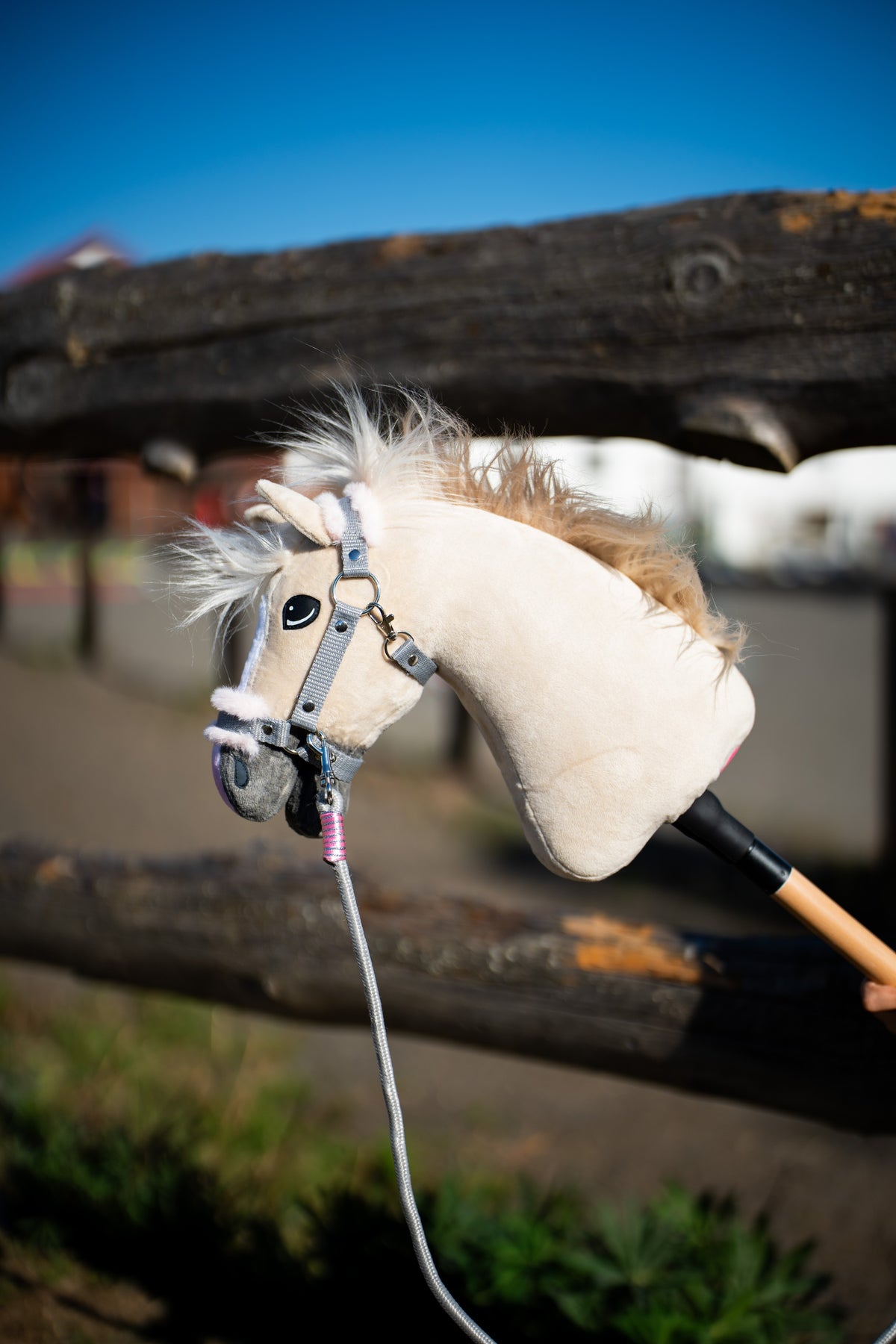 Hobby Horse Pixie ló egy rönkkerítés előtt szürke szőrmés kötőfékben és rózsaszín tekerésű szürke vezetőszárral
