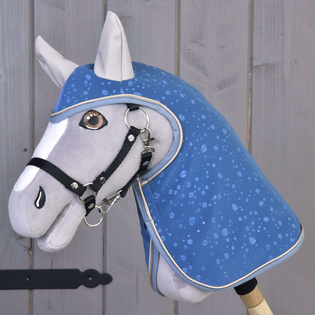 Szürke plüss Hobby Horse ló a kék, vízcseppmintás Dolly esőtakaróban, fekete kötőfékkel