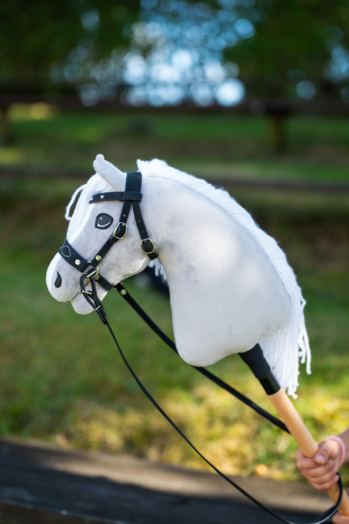 Hobby Horse Popcorn arany csatos fekete kantárban, díszített orrszíjjal és hosszú fekete szárral, mögötte zöld kert
