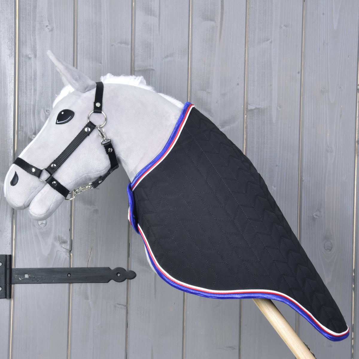 Szürke Hobby Horse ló oldalnézetből a fekete steppelt szállítótakaróban, amely az egész nyakat befedi egészen a fabotig