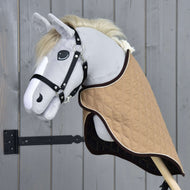 Szürke plüss Hobby Horse ló fekete kötőfékben, a bézs steppelt szállítótakaróban, elölről, háromnegyedes nézetből, szürke fafal mellett