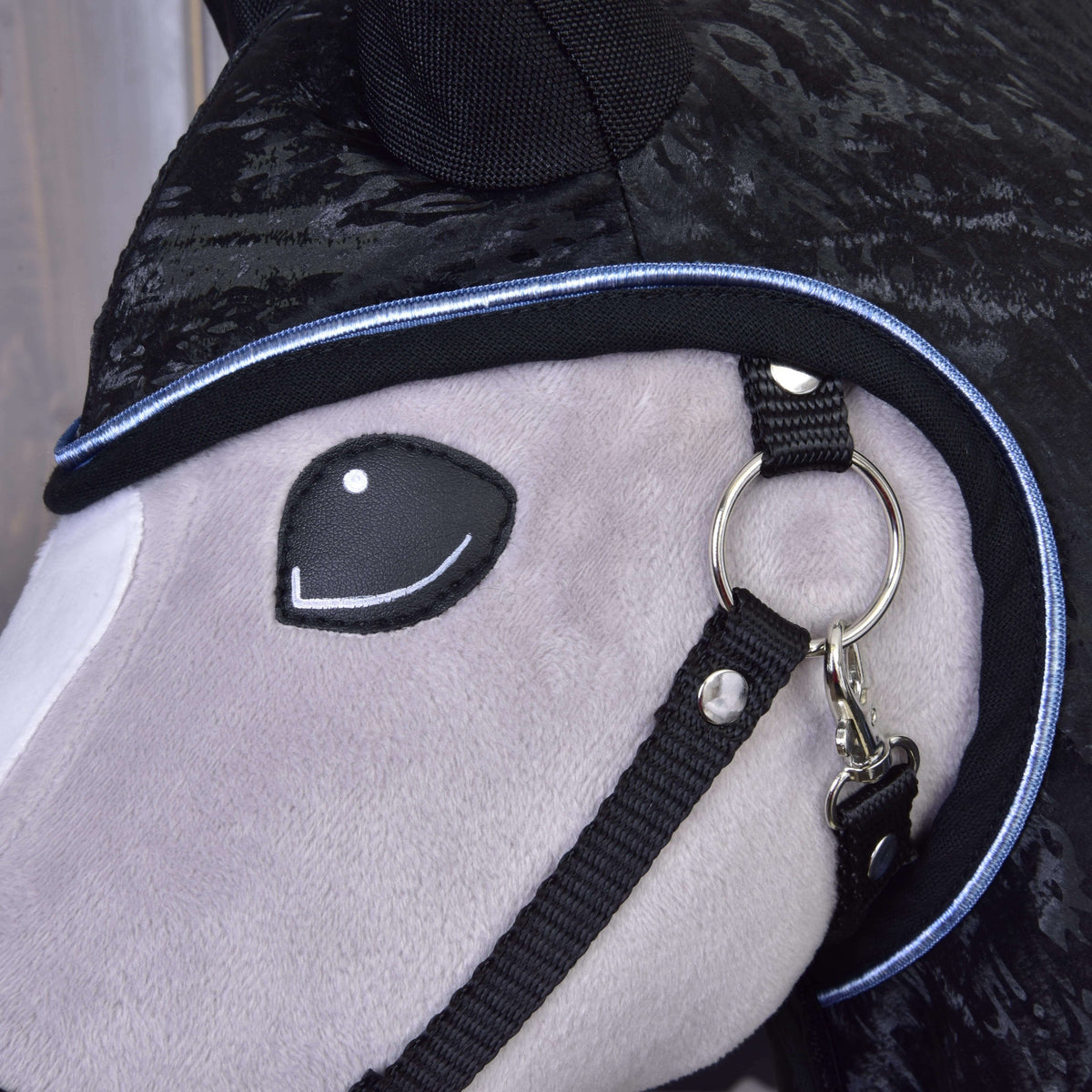 Close-up of the light blue piping around the head opening of the black raincoat by the black halter of a Hobby Horse