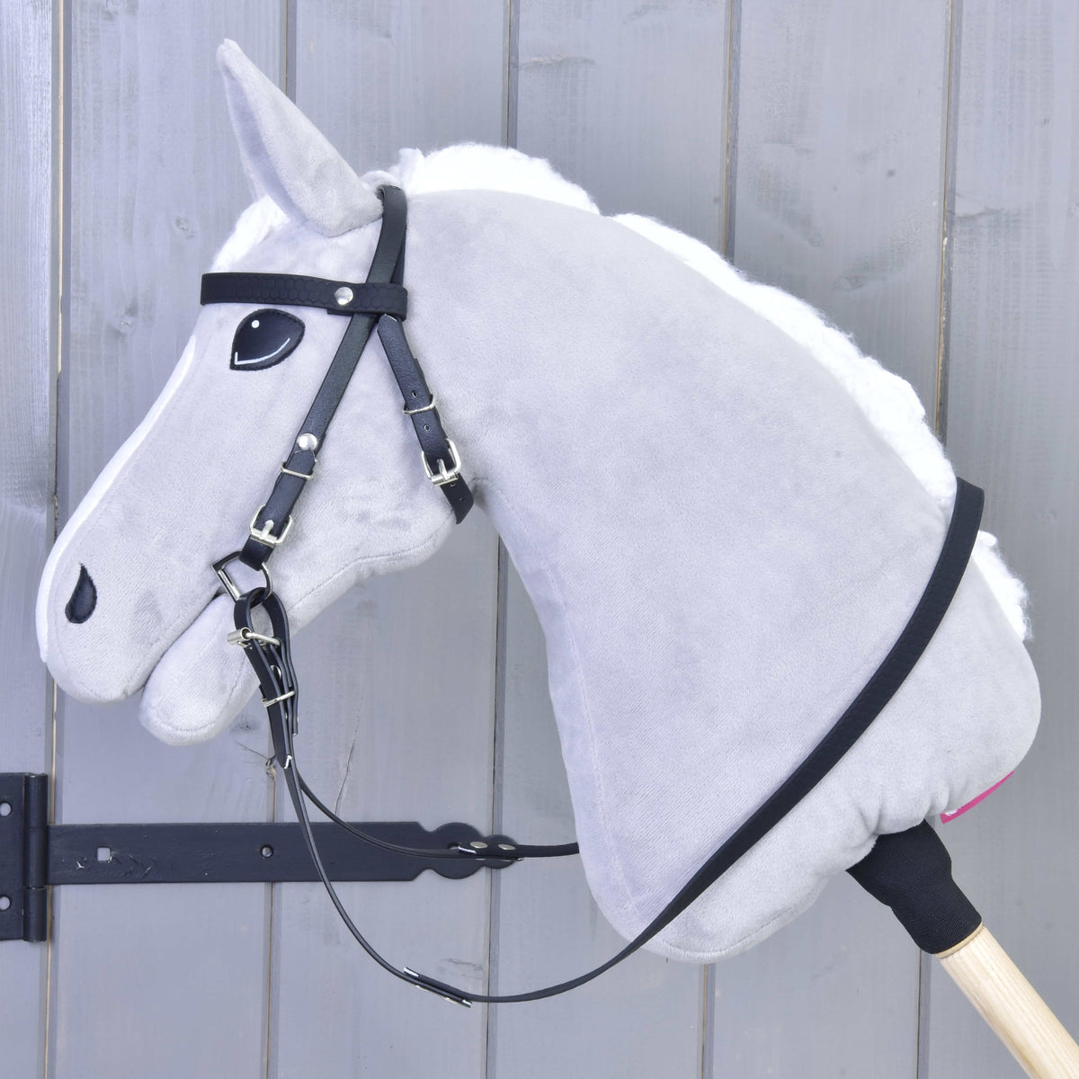 Szürke Hobby Horse ló bal profilból a fekete műbőr kantárban, a kantárszár a nyakán nyugszik