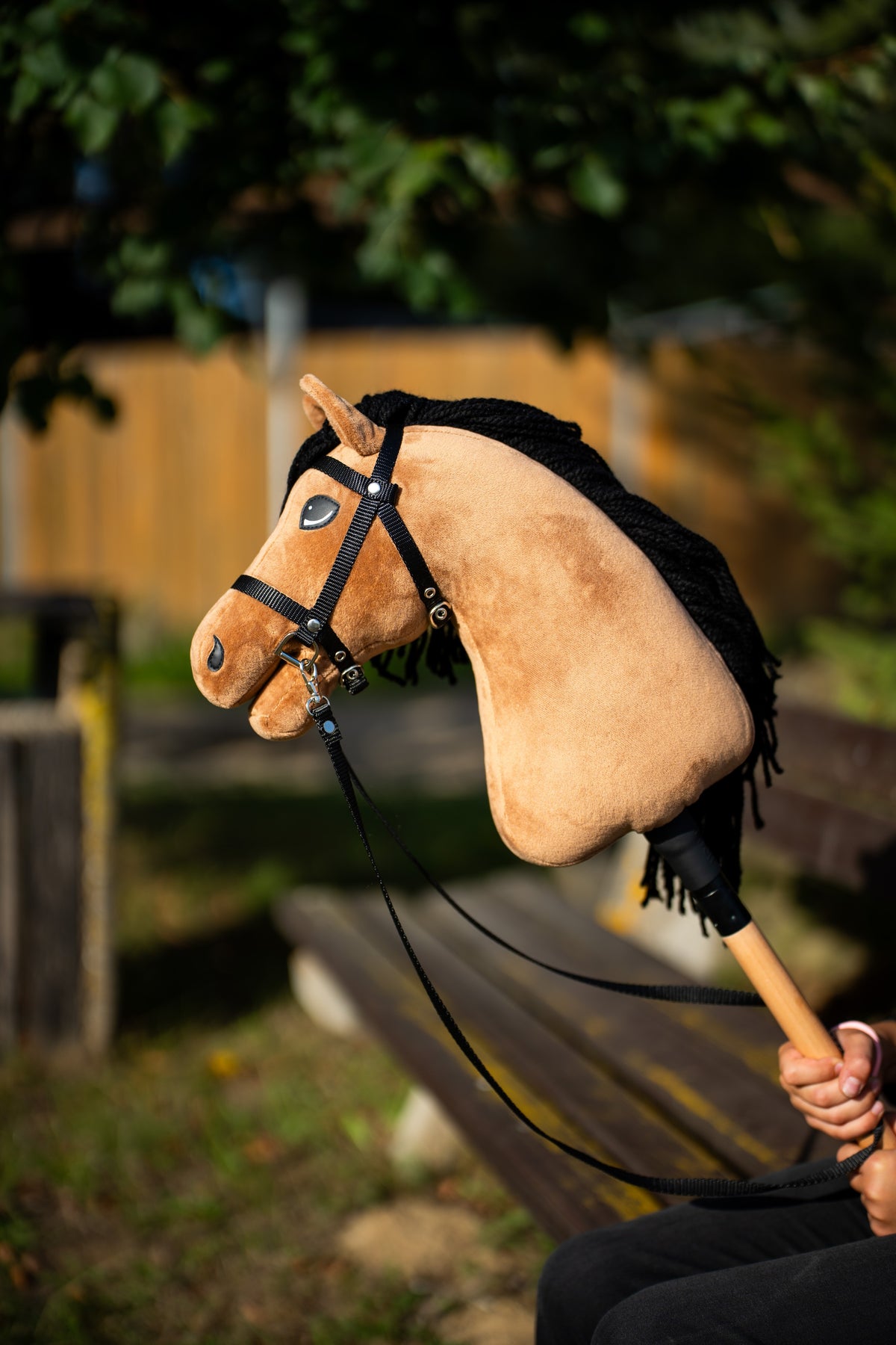 Hobby Horse Samantha with sandy plush and black yarn mane held up in warm evening light, wearing a black bridle