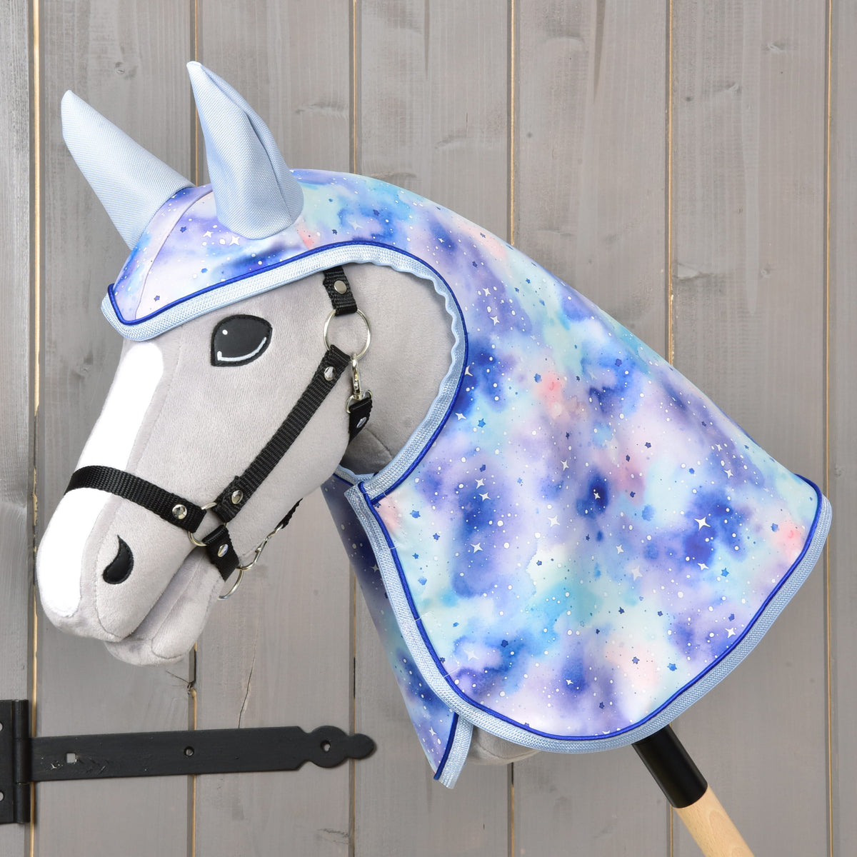 Szürke Hobby Horse ló fekete kötőfékben, a kék-lila galaxismintás Space esőtakaróban kapucnival és világoskék fülekkel