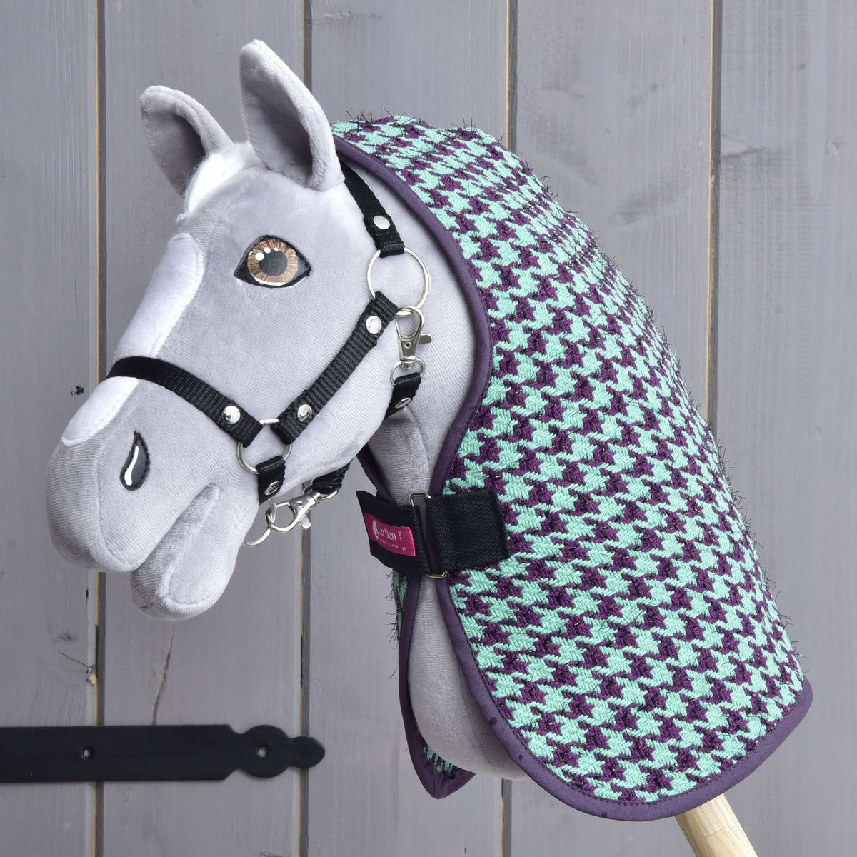 Barna szemű szürke Hobby Horse ló fekete kötőfékkel, rajta a zöld istállótakaró mentazöld-lila tyúklábmintával