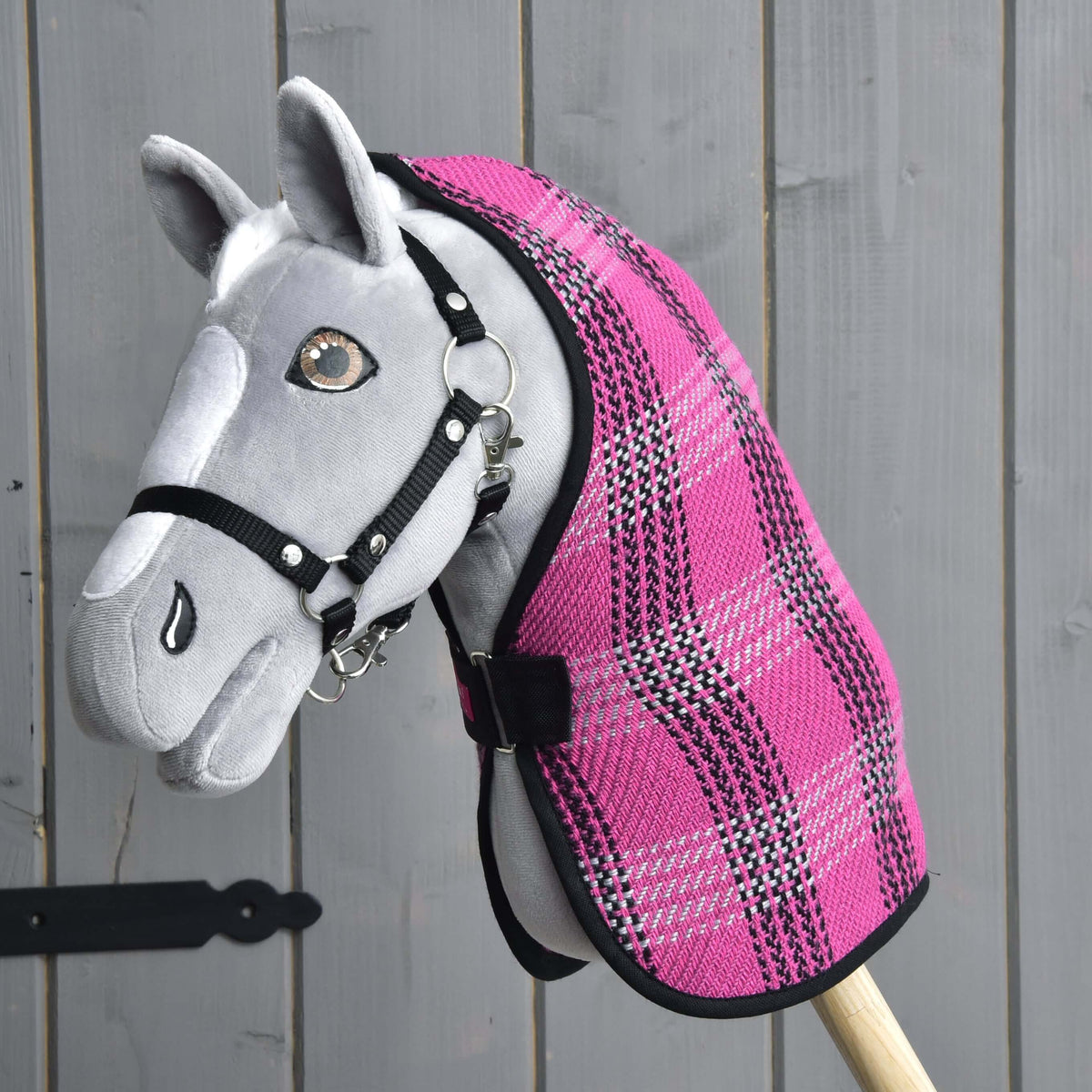 Barna szemű szürke Hobby Horse ló fekete kötőfékkel, rajta a rózsaszín istállótakaró rózsaszín-fekete-szürke kockás mintával