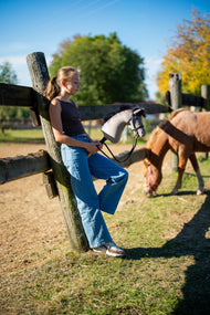Lány az őszi napsütésben egy karám kerítésének dőlve a fekete kantáros Hobby Horse Thor lóval, mögötte egy gesztenyebarna póni legel