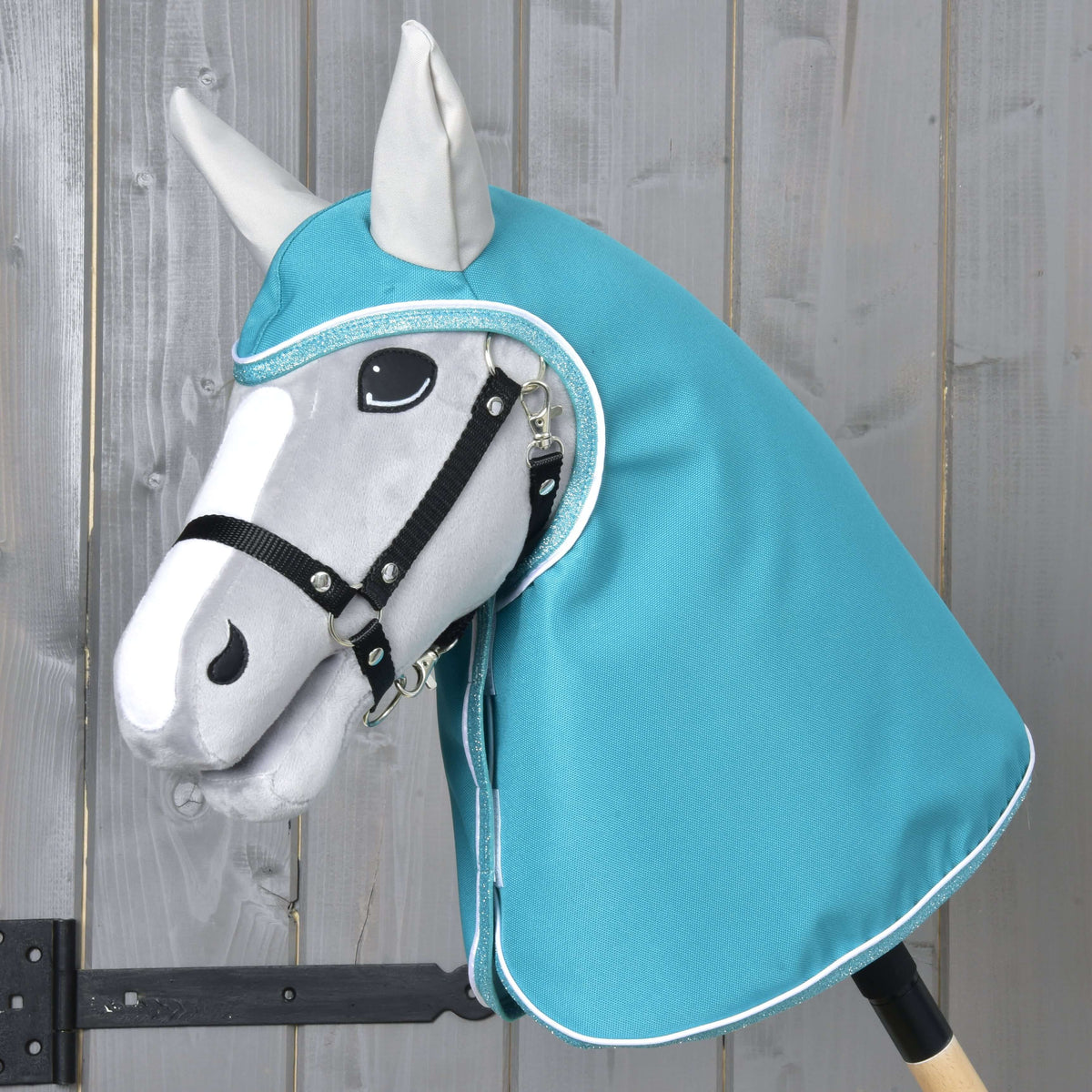 Grey Hobby Horse in a black halter wearing the Raincoat Turquoise with hood and light grey ears, covering head and neck