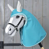 Szürke Hobby Horse ló fekete kötőfékben, a fejét és nyakát befedő kapucnis türkiz esőtakaróban, világosszürke fülekkel