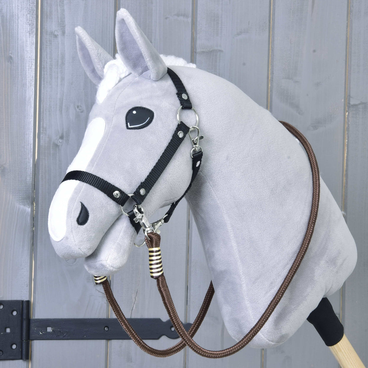 Világosszürke Hobby Horse ló fekete kötőfékben, a barna Vivaldi kantárszár az álla alatt bekapcsolva és a nyaka köré vetve