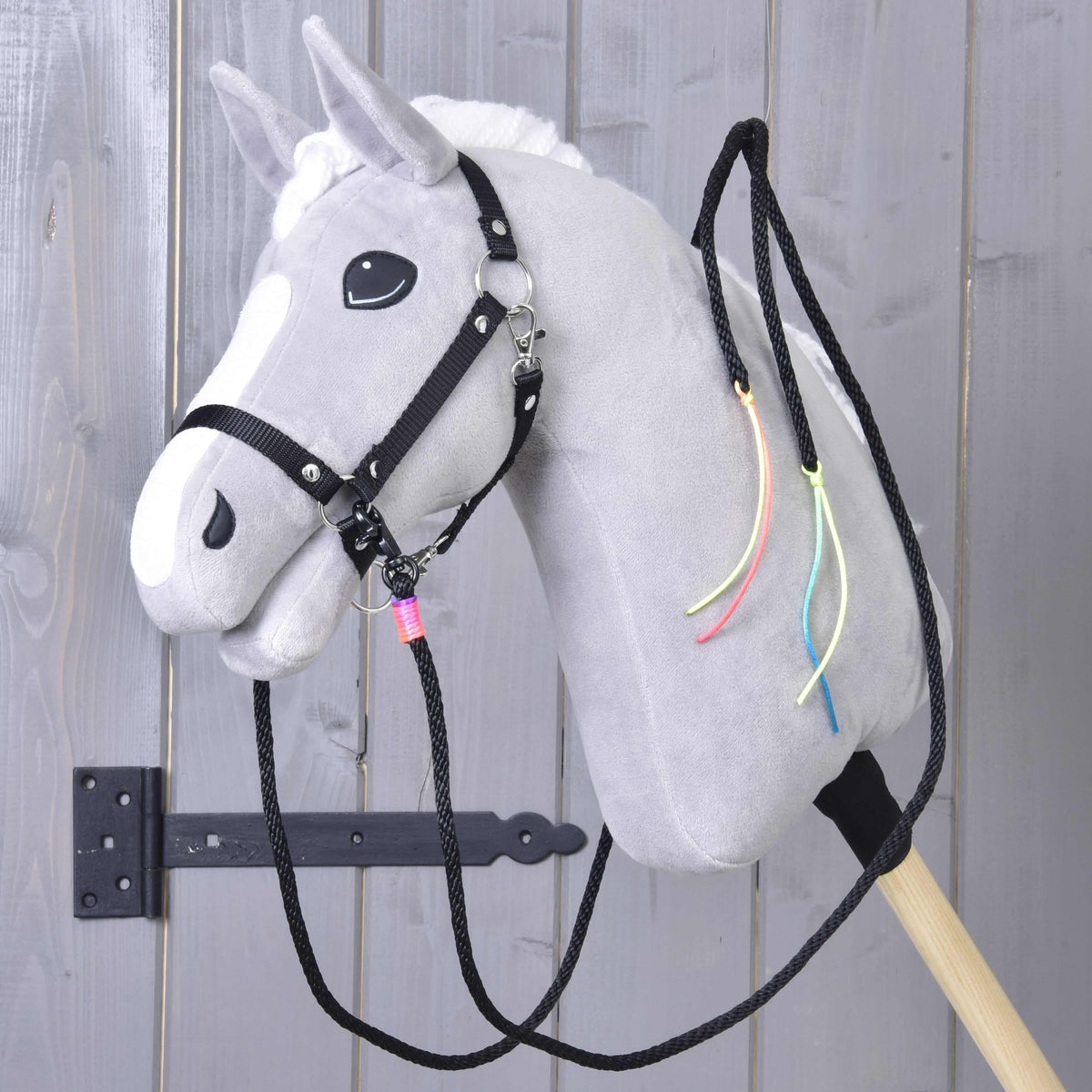 Szürke Hobby Horse ló fekete kötőfékben, fekete western kantárszárral, a nyakán neon zsinórbojtok lógnak