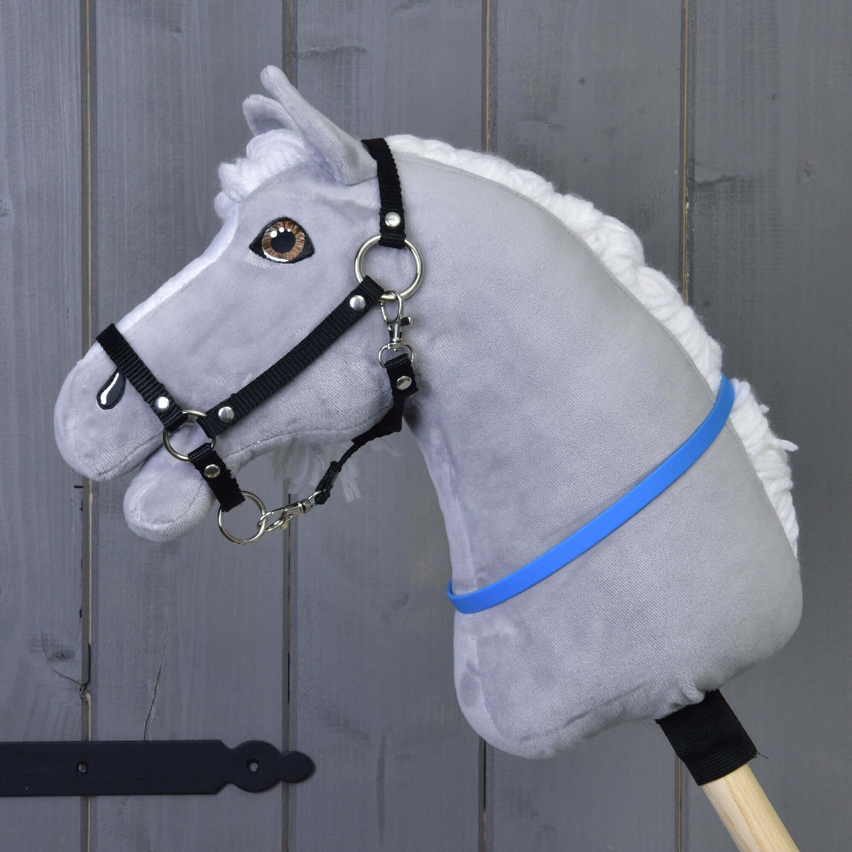 Szürke plüss Hobby Horse ló fehér sörénnyel és fekete kötőfékkel, a nyakán az élénkkék nyakgyűrű (cordeo)