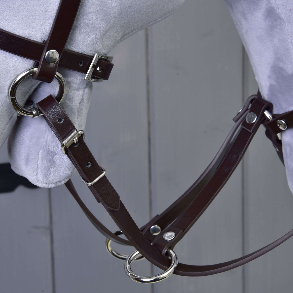 Close-up of the dark brown leatherette martingale with silver rings and the reins on a grey Hobby Horse