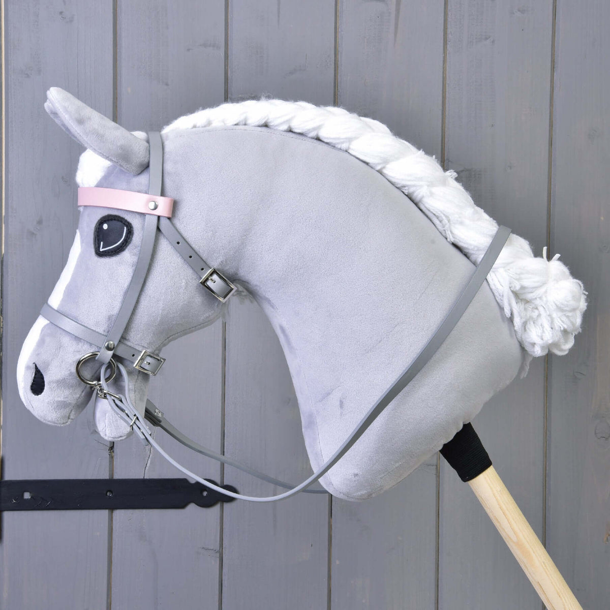 Grey plush Hobby Horse with a braided white mane wearing the grey leatherette bridle and reins, side view