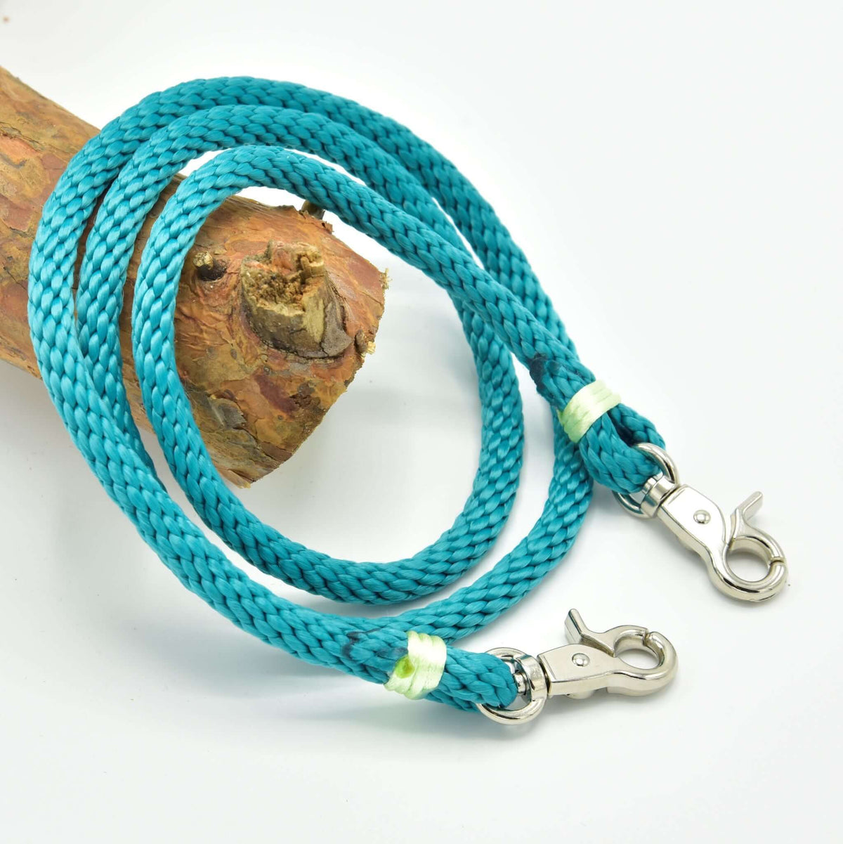 LarDen Hobby Horse Reins Turquoise in braided rope with pale green wraps and silver snap hooks on a branch